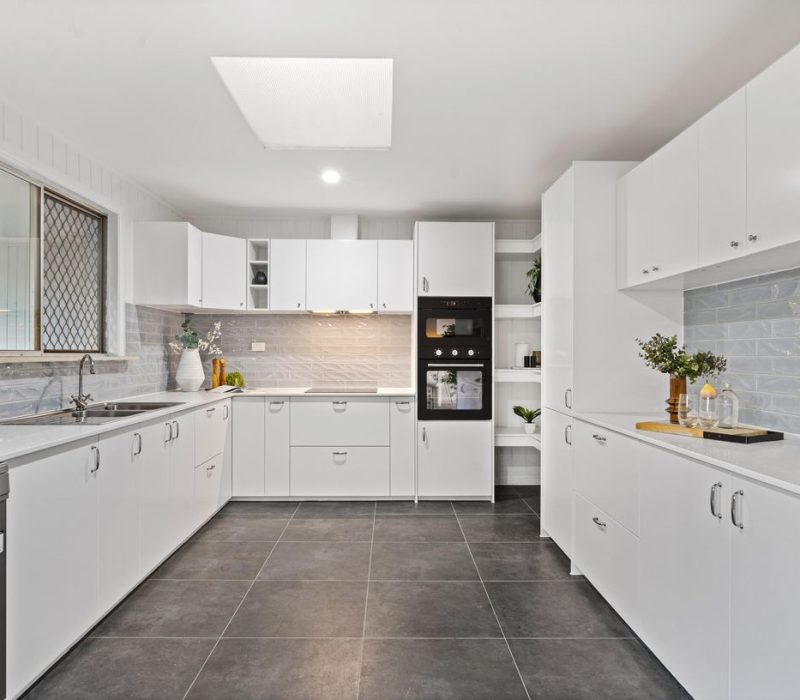Spacious white kitchen with modern grey tile floors and soft blue splashback