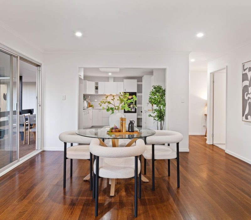 Dining area with glass table and view into modern white kitchen